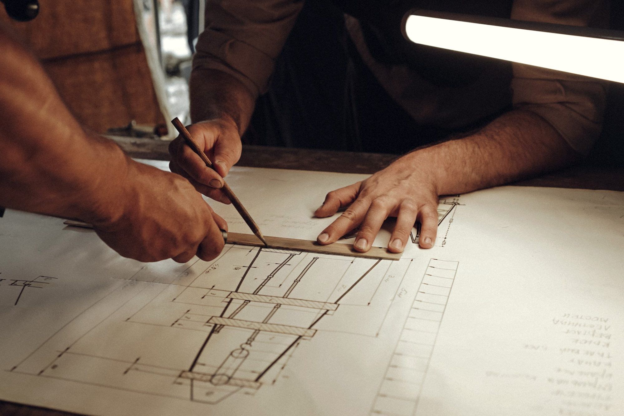 Hands drafting an engineering drawing with a scale rule